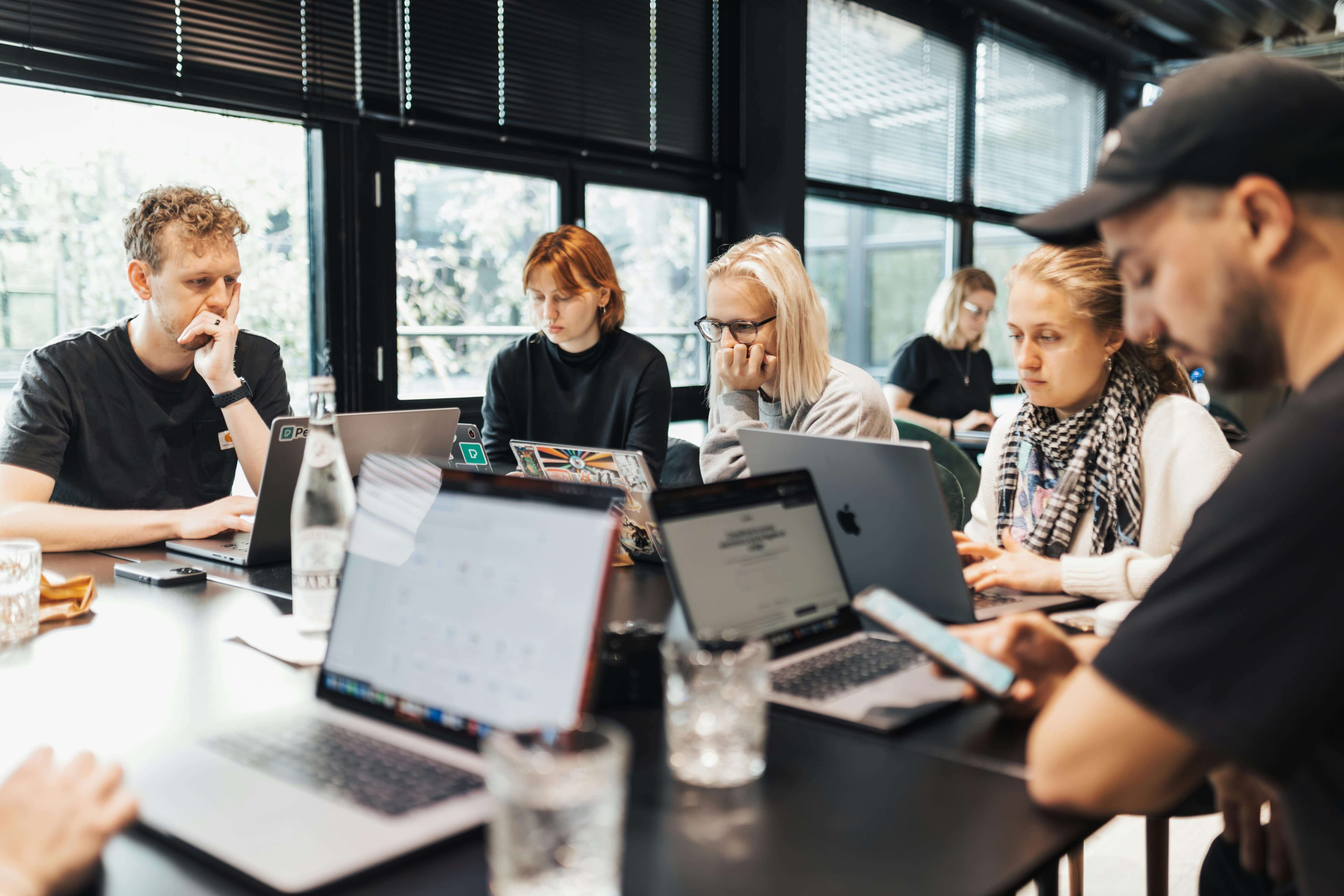 A diverse engineering team working on laptops around a shared table in a bright, modern coworking space.