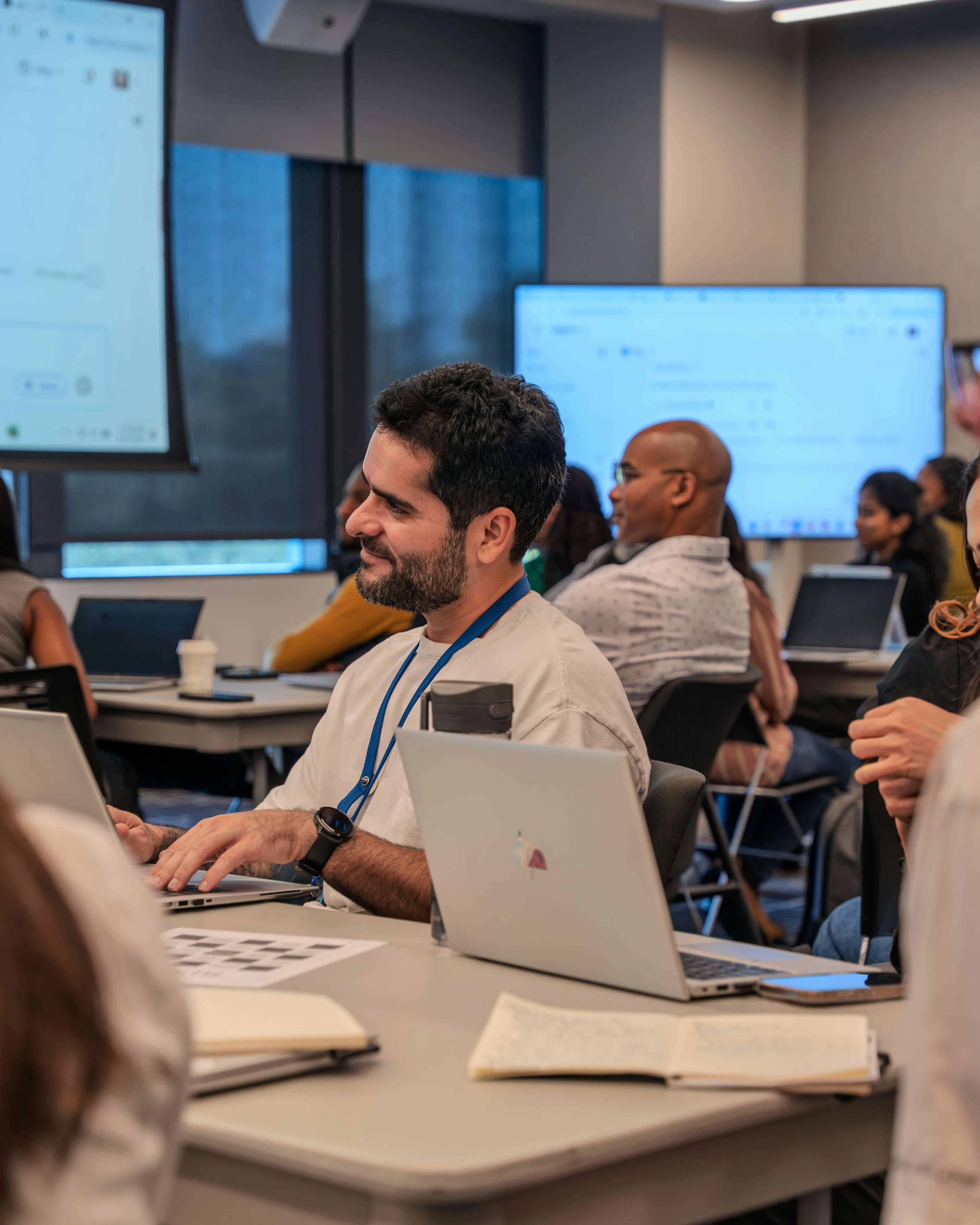 A smiling senior engineer working at a laptop during a collaborative working session with diverse teammates in the background.